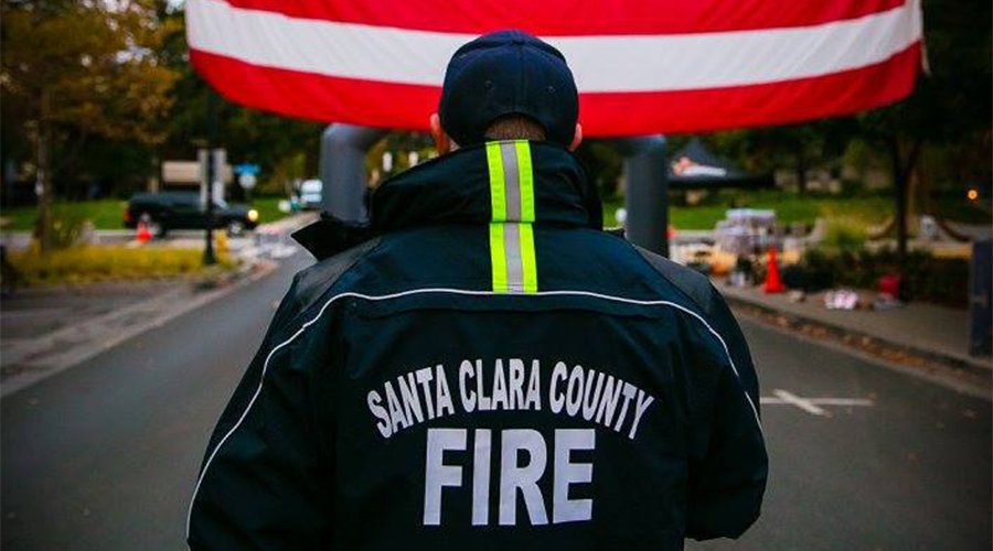 Man wearing Santa Clara County Fire jacket with American Flag in background